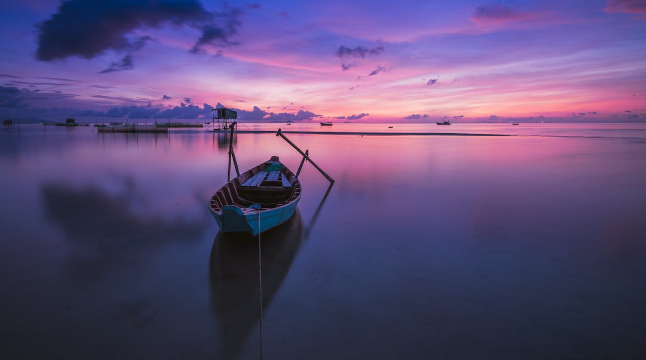 A tranquil sunrise over a tropical ocean with a solitary boat reflecting peaceful hues.