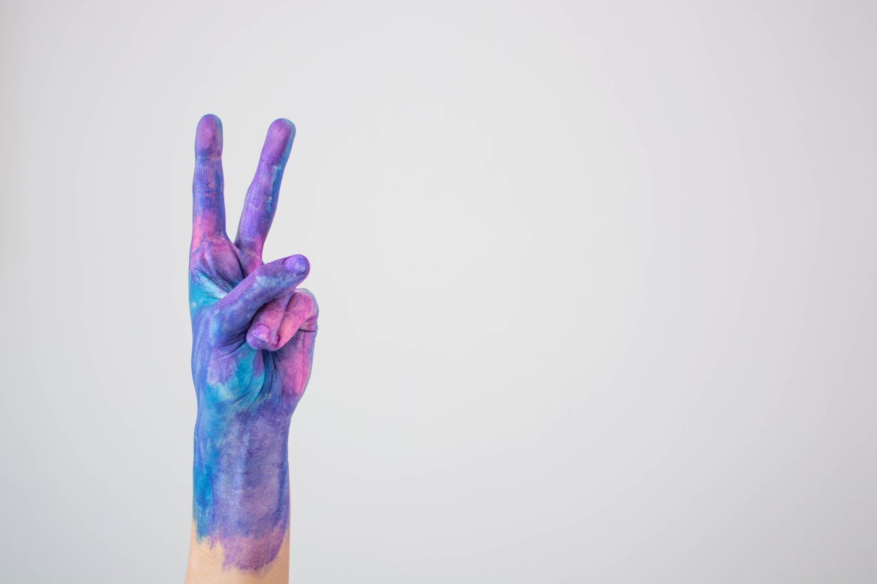 Vividly painted hand making a peace sign against a plain background.